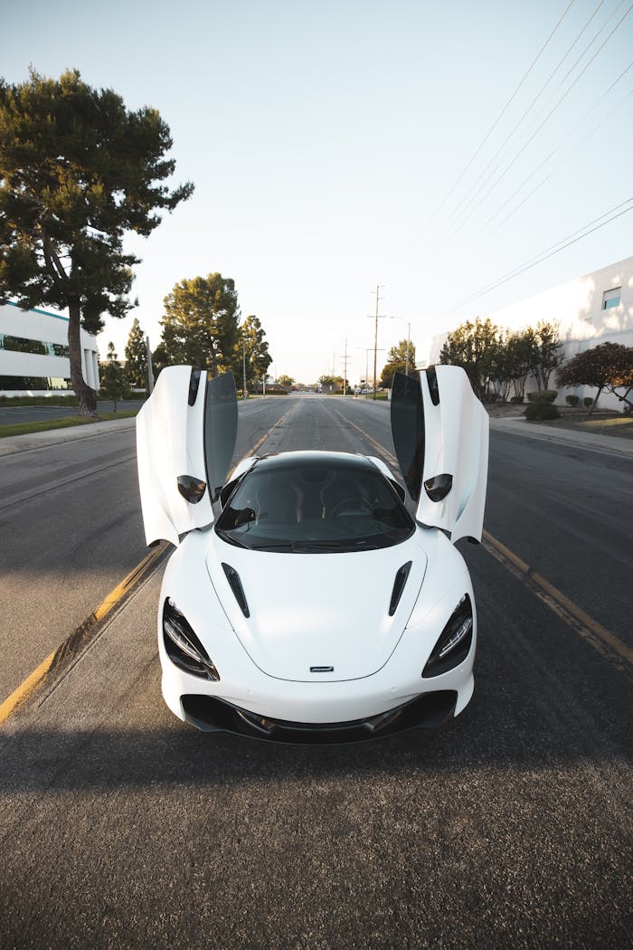 A sleek white supercar parked on a suburban road with its doors open, showcasing its modern design under a clear sky.